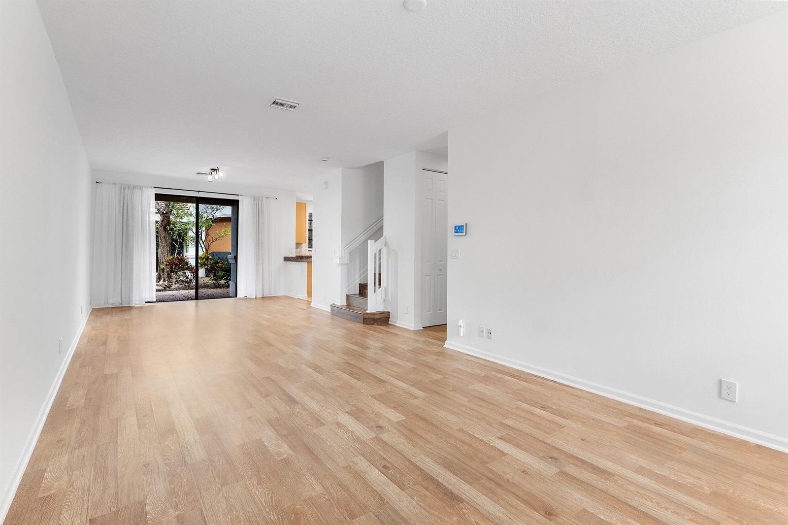 An empty living room features light wood flooring, white walls, a staircase, and sliding glass doors — 238 E Chrystie Circle, Delray Beach FL 33484, DELRAY BEACH, FL