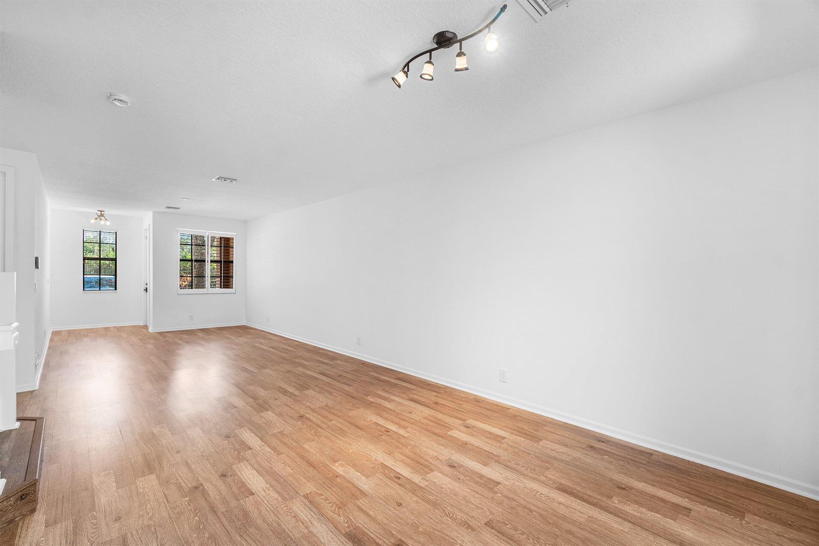 An empty living room features white walls, wood-look flooring, and a modern track light fixture — 238 E Chrystie Circle, Delray Beach FL 33484, DELRAY BEACH, FL