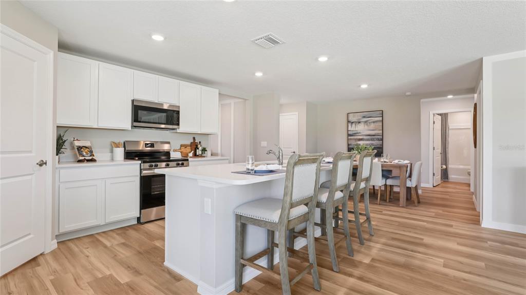 A modern kitchen features white cabinets, a central island with bar seating, and wood flooring — 2074 NE 28TH PLACE, OCALA, FL