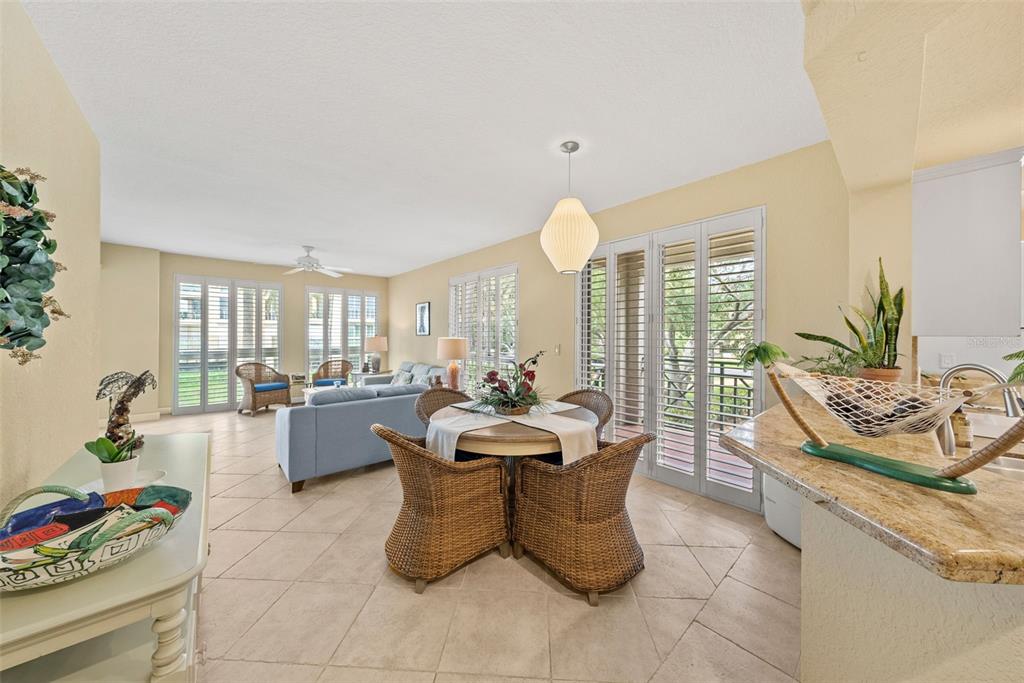 An open-concept living and dining area features tile floors, wicker furniture, and plantation shutters — 4780 DOLPHIN CAY LANE S UNIT 109, ST PETERSBURG, FL