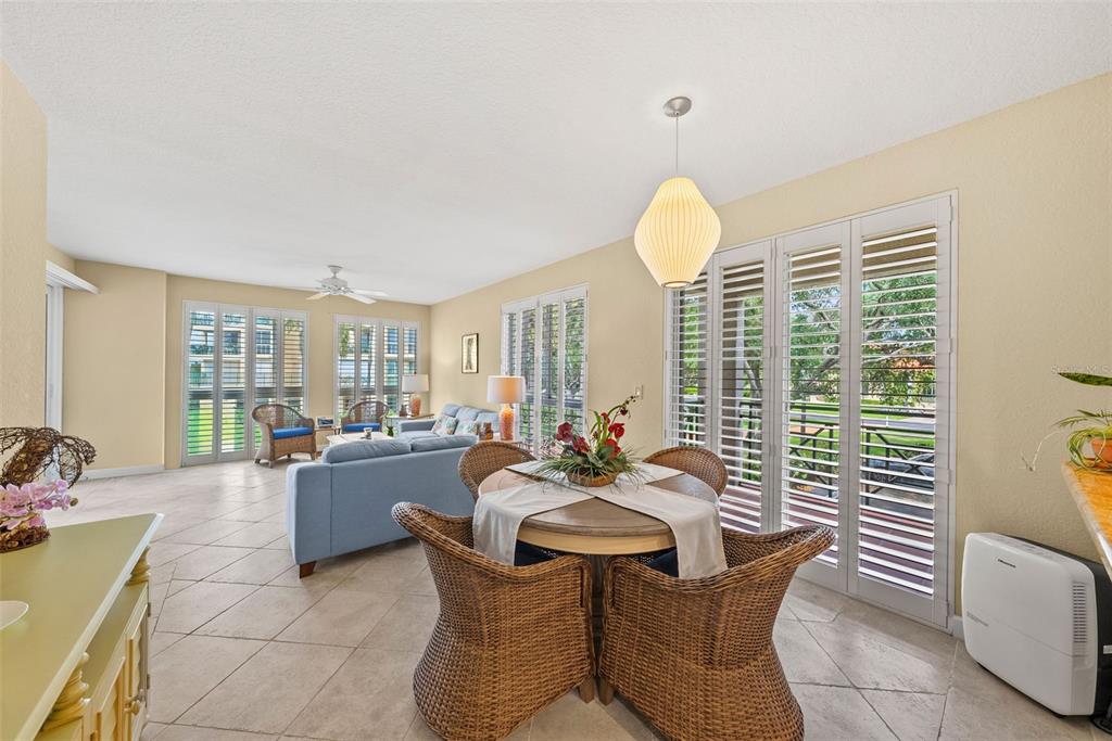 A bright living and dining area features tile floors, wicker furniture, and plantation shutters — 4780 DOLPHIN CAY LANE S UNIT 109, ST PETERSBURG, FL