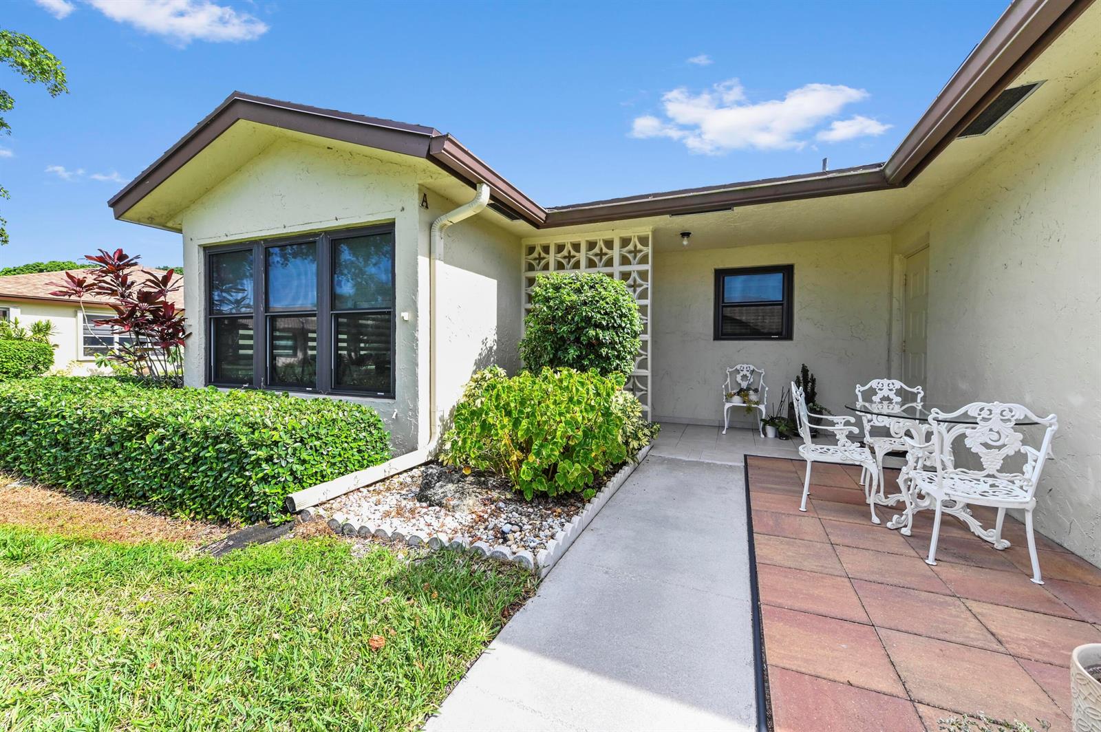 A beige house exterior features a tiled patio, white metal furniture, and a landscaped garden — 14080 Nesting Way # A, Delray Beach FL 33484, DELRAY BEACH, FL