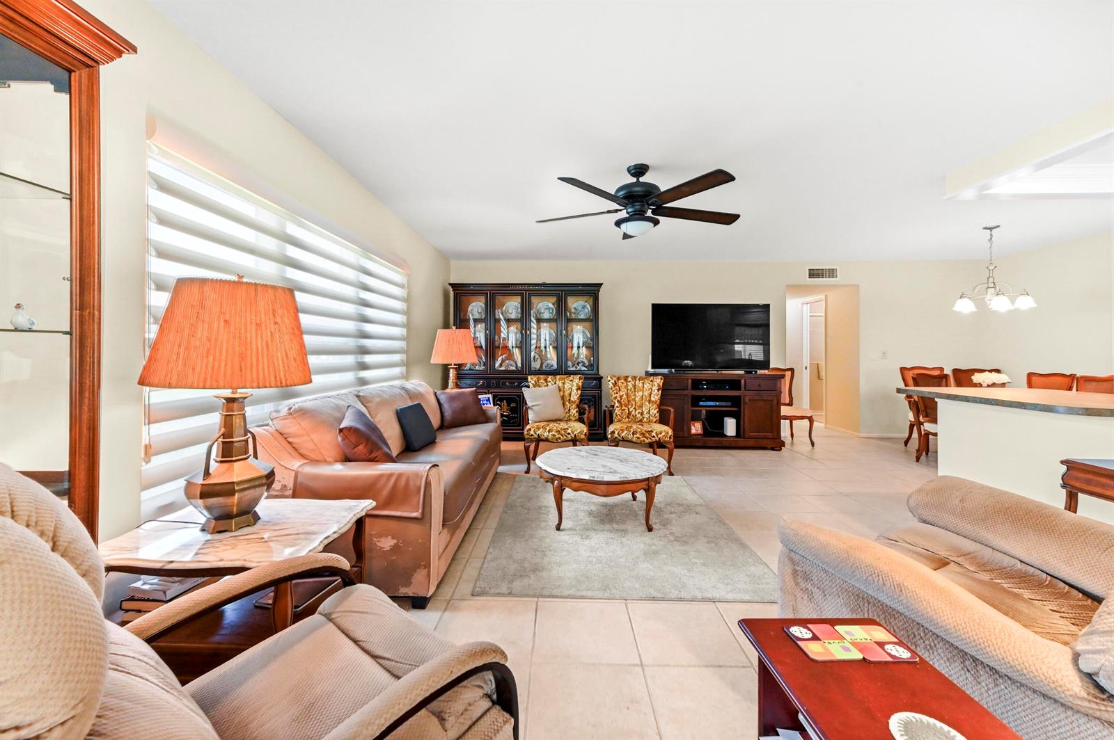 A living room features a leather sofa, two patterned armchairs, a television, and tile flooring — 14080 Nesting Way # A, Delray Beach FL 33484, DELRAY BEACH, FL