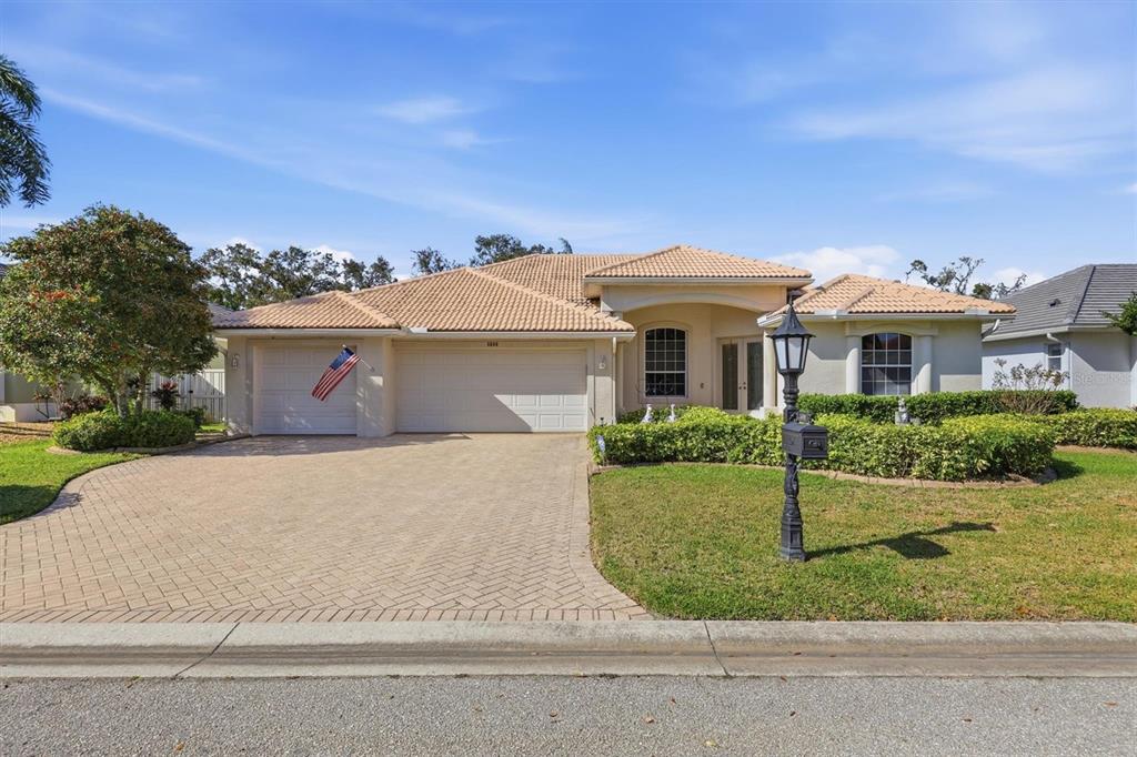 A single-story house with a beige stucco exterior, tile roof, and a paved driveway — 5608 EASTWIND DRIVE, SARASOTA, FL