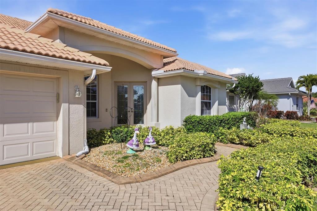A beige house exterior features a paved driveway, a garage, and a landscaped front garden — 5608 EASTWIND DRIVE, SARASOTA, FL