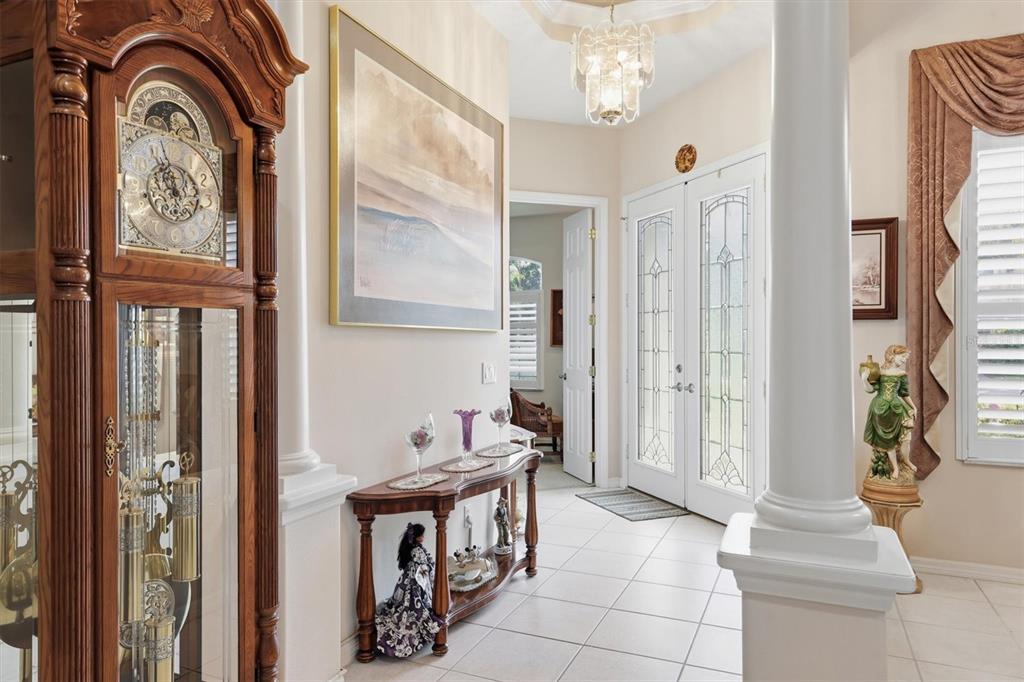 A tiled entryway features a grandfather clock, a console table, and white columns — 5608 EASTWIND DRIVE, SARASOTA, FL