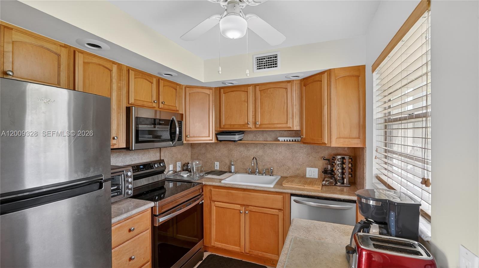 A kitchen features wood cabinets, stainless steel appliances, a white sink, and a ceiling fan — 438 Mansfield K # 438, Boca Raton FL 33434, BOCA RATON, FL