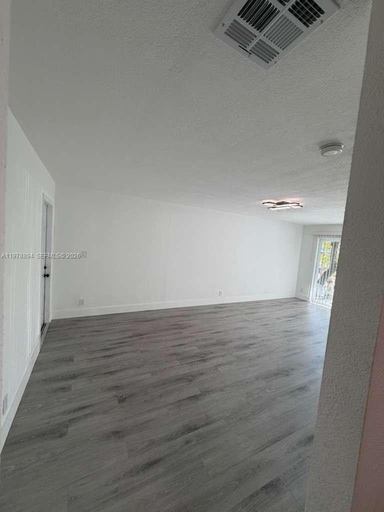 An empty room features white walls, gray wood-look flooring, and a sliding glass door — 4271 NW 5th St # 129, Plantation FL 33317, PLANTATION, FL