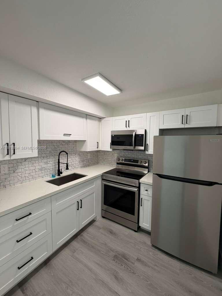 A modern kitchen features white cabinets, stainless steel appliances, and a gray subway tile backsplash — 4271 NW 5th St # 129, Plantation FL 33317, PLANTATION, FL