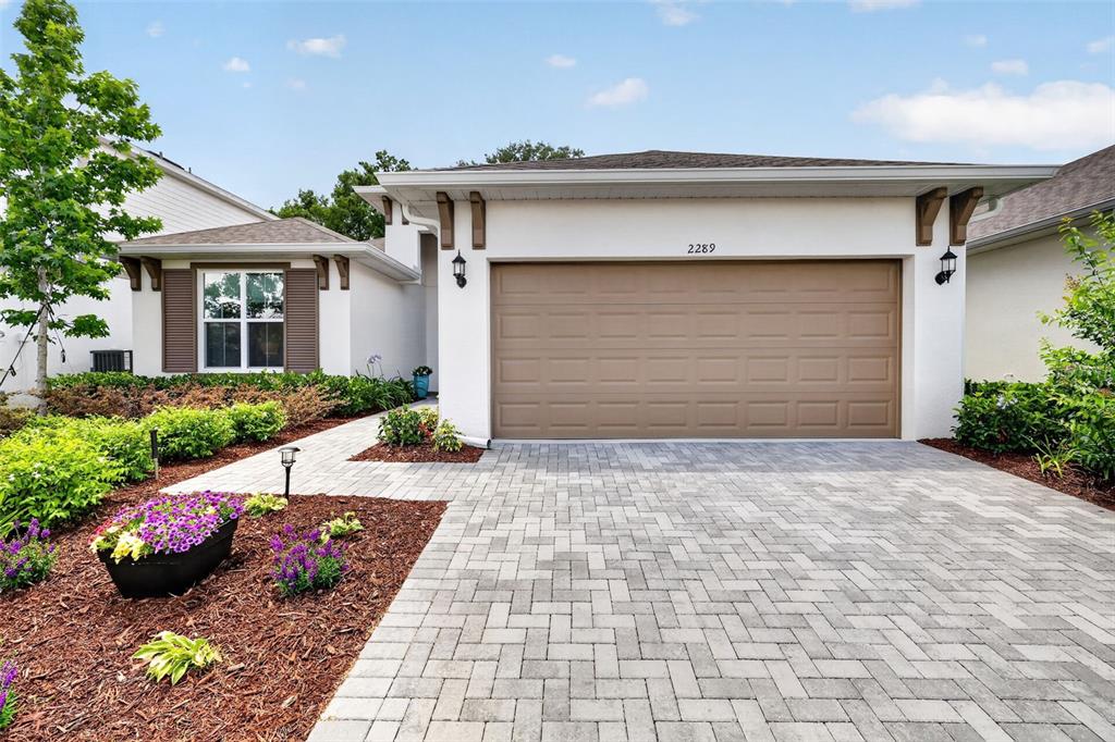 A single-story house with a tan garage door, white stucco walls, and a paver driveway — 2289 SIRENA LANE, MOUNT DORA, FL