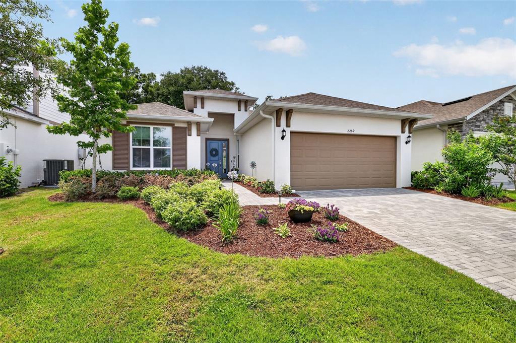 A single-story house with a tan stucco exterior, a brown garage door, and a landscaped yard — 2289 SIRENA LANE, MOUNT DORA, FL