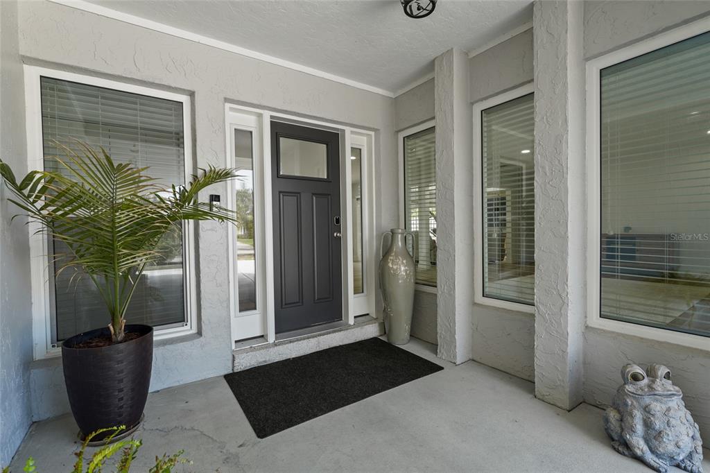 A gray front door with a window sits between large windows on a covered porch — 138 HOLLY AVENUE, SARASOTA, FL