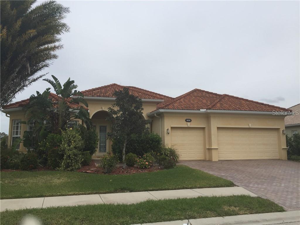 A single-story house with a terracotta tile roof, beige stucco exterior, and a three-car garage — 5570 ROCK DOVE DRIVE, SARASOTA, FL
