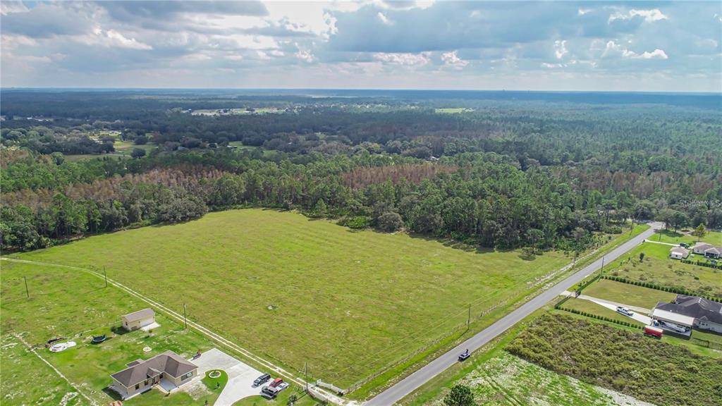 An aerial view shows a large, grassy vacant lot bordered by a road and trees — SAN JUAN AVENUE, POLK CITY, FL