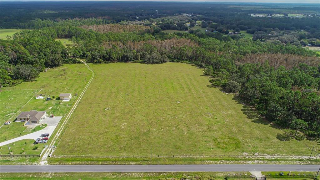 An aerial view shows a large, grassy lot adjacent to a house and wooded area — SAN JUAN AVENUE, POLK CITY, FL