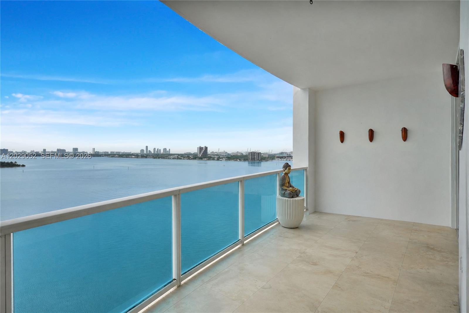 A balcony with a glass railing overlooks a bay with a distant city skyline — 725 NE 22nd St # 11E, Miami FL 33137, MIAMI, FL