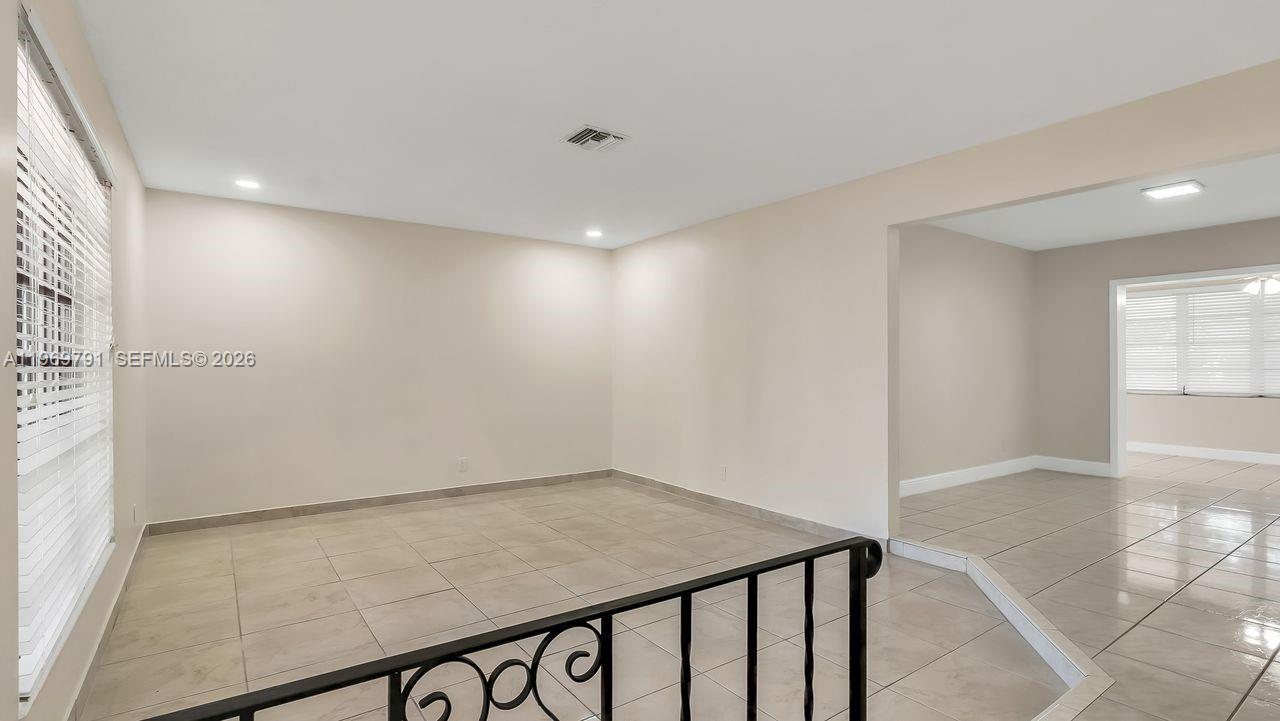 A room with light-colored tile flooring and a black metal railing in the foreground — 5300 Grant St, Hollywood FL 33021, HOLLYWOOD, FL