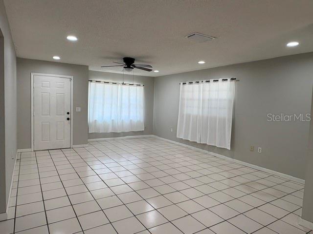 An empty living room features white tile flooring, gray walls, recessed lighting, and two windows — 506 W 9TH STREET, FROSTPROOF, FL