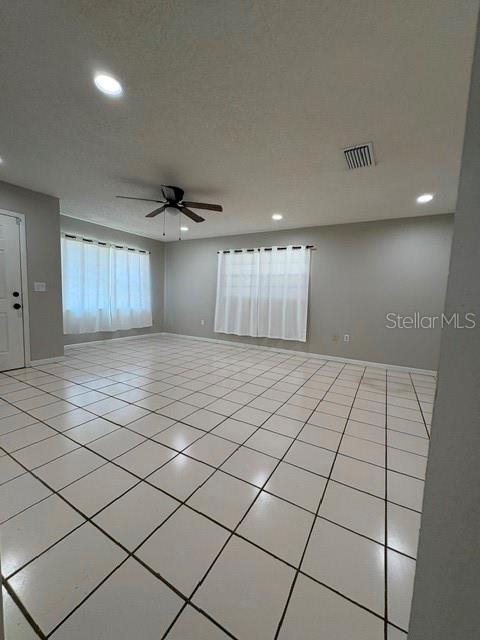 A spacious, empty room features white tiled floors, a ceiling fan, and large window curtains — 506 W 9TH STREET, FROSTPROOF, FL