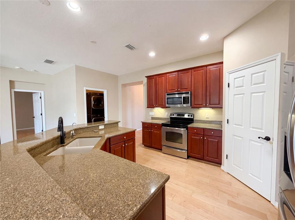 A kitchen features cherry wood cabinets, granite countertops, stainless steel appliances, and light wood flooring — 5605 WINDSONG OAK DRIVE, LEESBURG, FL
