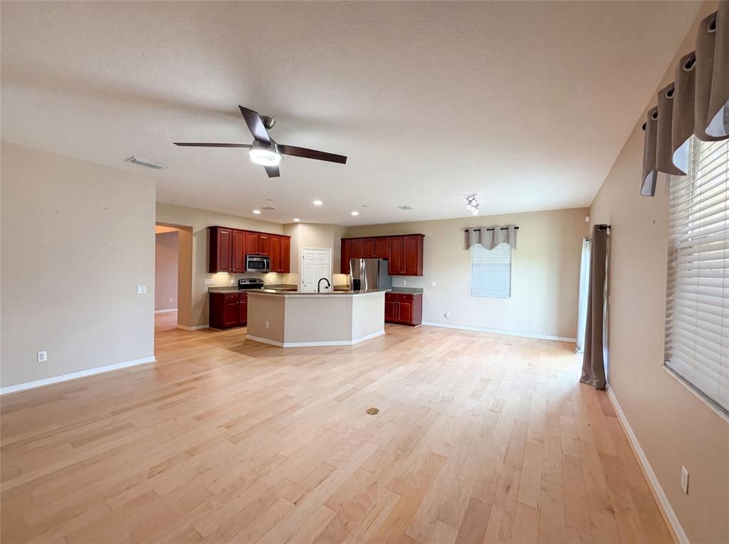 An open-concept kitchen with dark wood cabinets and a central island overlooks a living area — 5605 WINDSONG OAK DRIVE, LEESBURG, FL