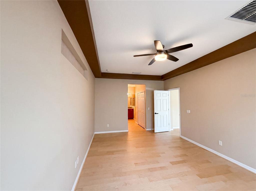 An empty bedroom features light wood flooring, a tray ceiling with a fan, and white doors — 5605 WINDSONG OAK DRIVE, LEESBURG, FL
