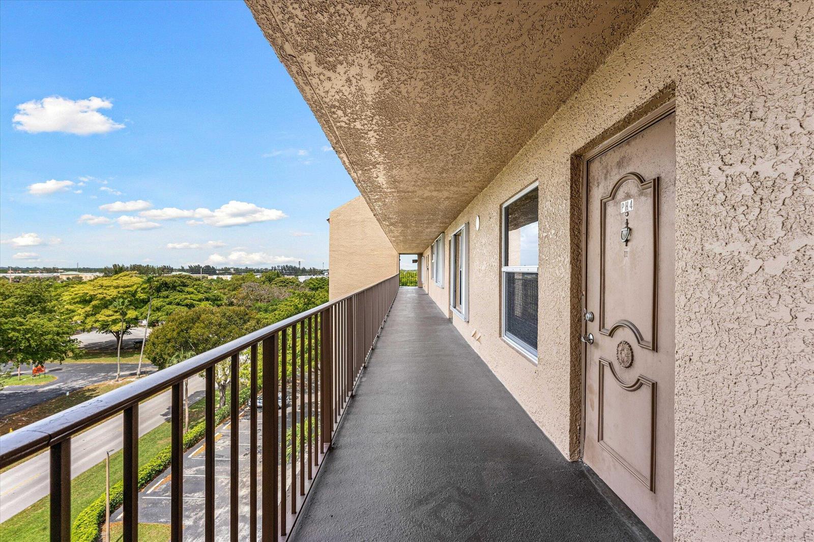 An exterior walkway with a metal railing overlooks a parking lot and trees — 4570 NW 18th Avenue # 704, Deerfield Beach FL 33064, DEERFIELD BEACH, FL