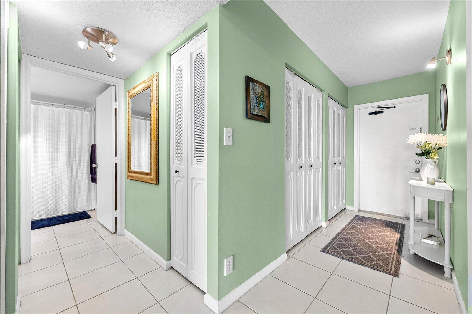 A hallway with light green walls, white tile flooring, and several white louvered closet doors — 4570 NW 18th Avenue # 704, Deerfield Beach FL 33064, DEERFIELD BEACH, FL