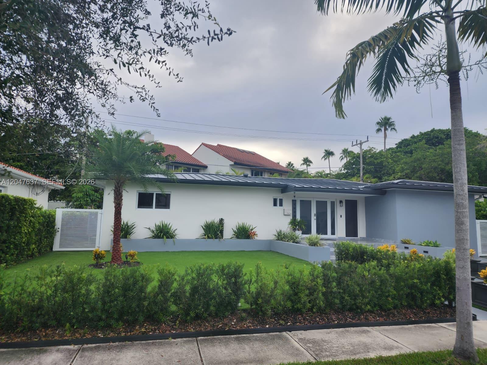 A single-story white house with a metal roof, front lawn, and landscaping under a cloudy sky — 3504 Crystal View Ct # 0, Miami FL 33133, MIAMI, FL