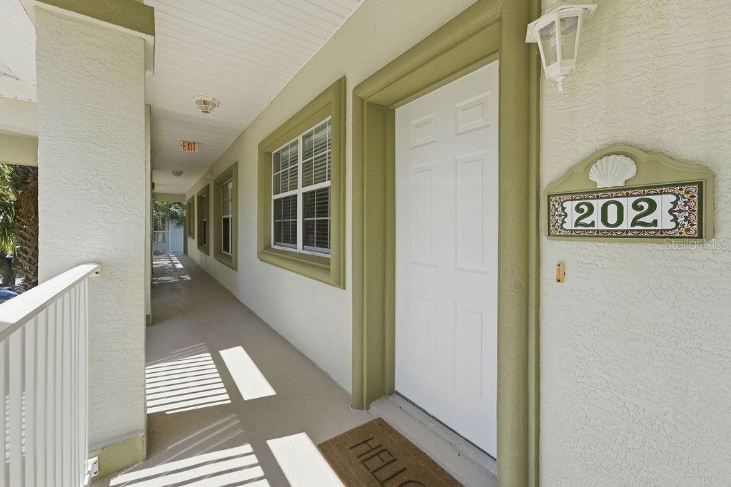 An exterior hallway features a white door labeled 202 with a decorative shell plaque above — 90 SAN JUAN DRIVE UNIT B202, PALM COAST, FL