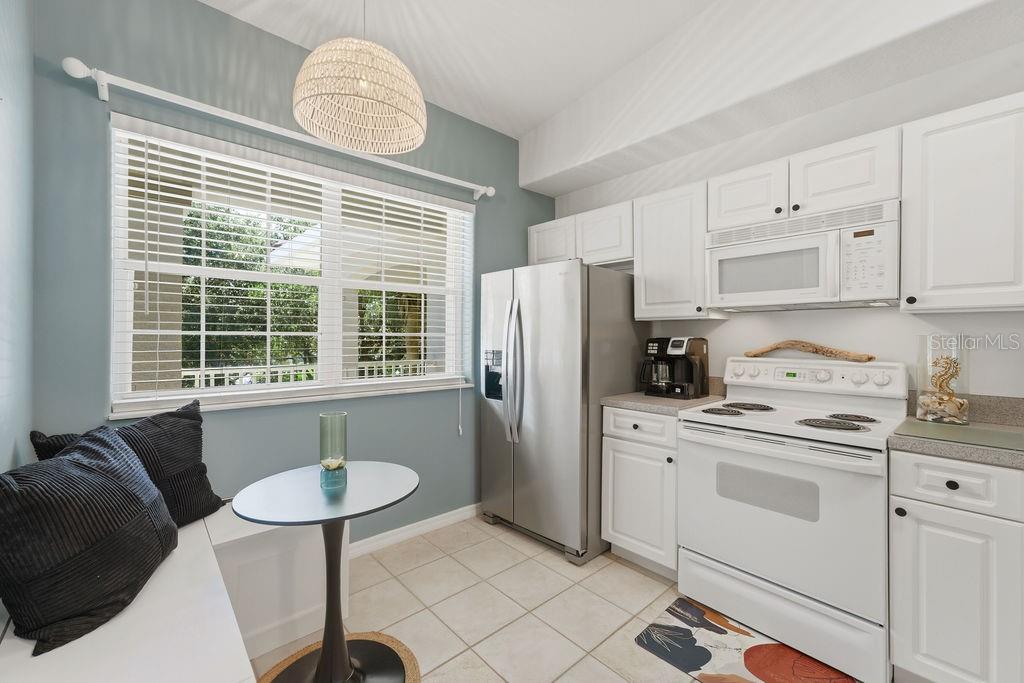 A kitchen with white cabinets, stainless steel appliances, a small dining nook, and blue walls — 90 SAN JUAN DRIVE UNIT B202, PALM COAST, FL