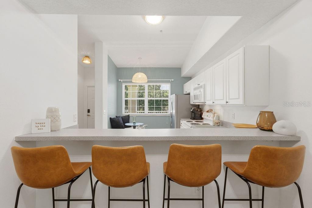 A kitchen with a breakfast bar, four tan stools, white cabinets, and a dining nook — 90 SAN JUAN DRIVE UNIT B202, PALM COAST, FL