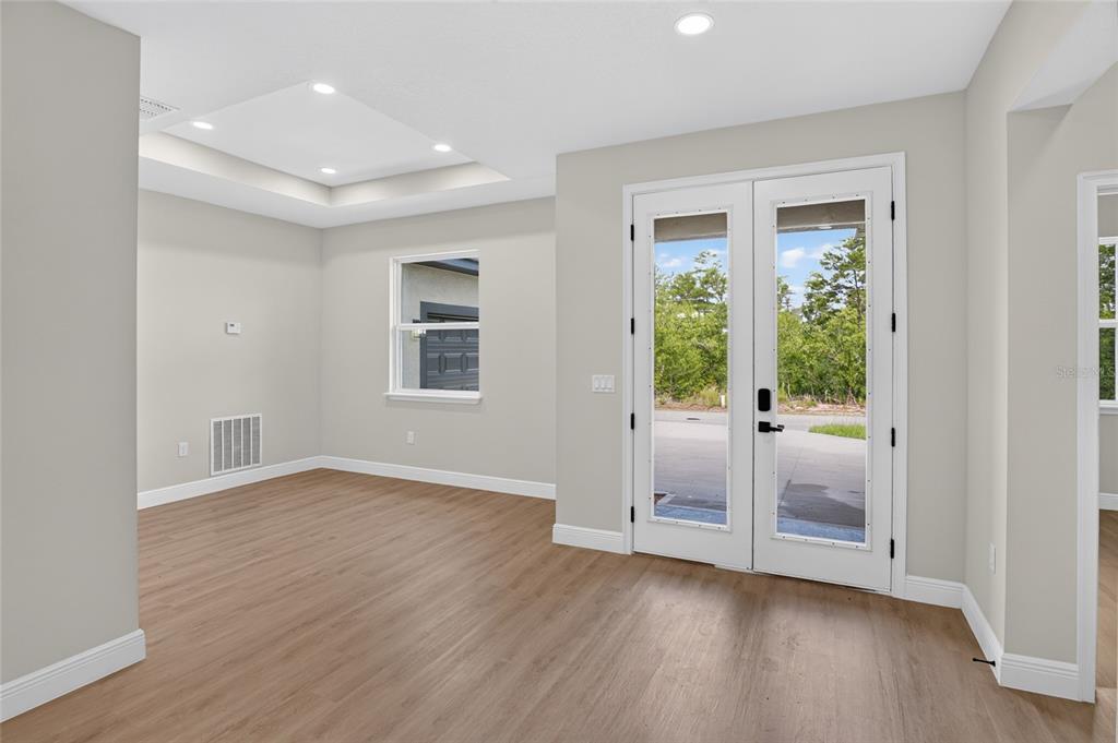 A room with light-colored walls, wood-look flooring, a tray ceiling, and double glass doors — 4 LONE PINE STREET, HOMOSASSA, FL