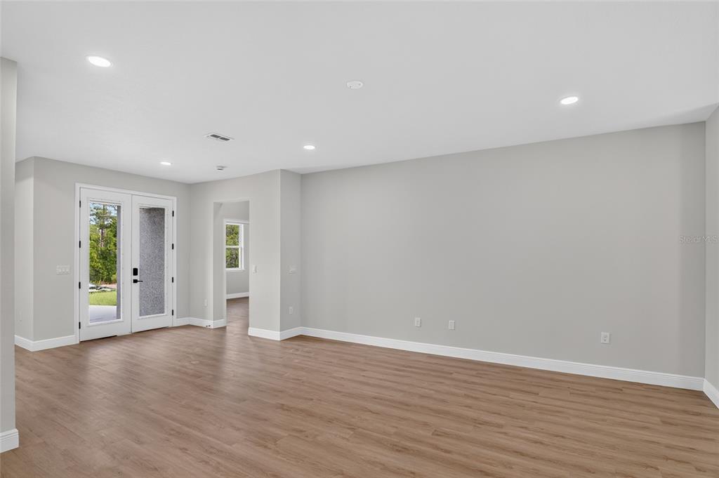 An empty room with light wood-look flooring, gray walls, recessed lighting, and glass double doors — 4 LONE PINE STREET, HOMOSASSA, FL