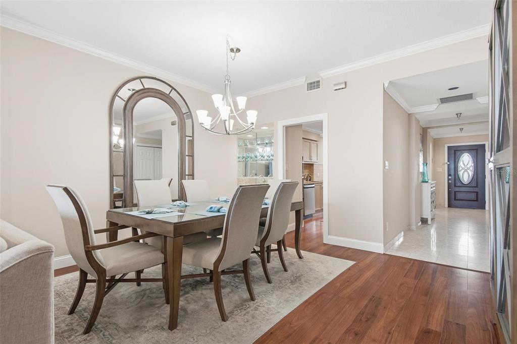 A dining room with a glass-top table, upholstered chairs, a large arched mirror, and chandelier — 11 AVENUE DE LA MER UNIT 1306, PALM COAST, FL