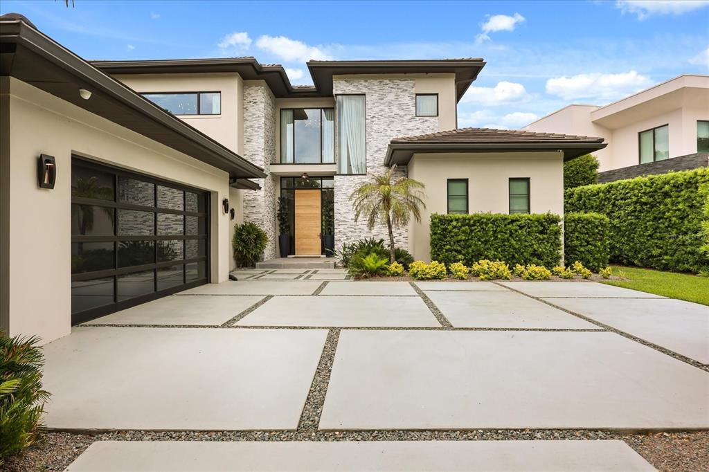 A modern two-story house features a stone facade, a glass garage door, and a concrete driveway — 10348 KENSINGTON SHORE DRIVE, ORLANDO, FL