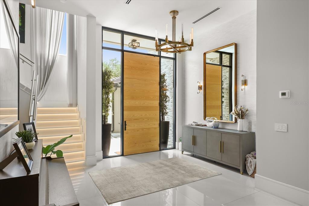 A modern entryway features a large wooden door, a chandelier, a console table, and stairs — 10348 KENSINGTON SHORE DRIVE, ORLANDO, FL
