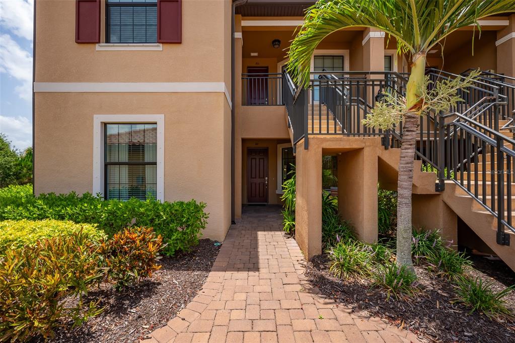 A tan stucco building exterior features a brick walkway, stairs, and a palm tree — 5425 CICERONE STREET UNIT 101, SARASOTA, FL