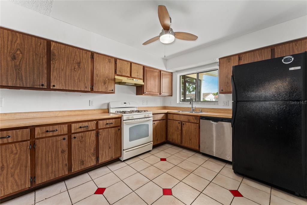 A kitchen features wood cabinets, white appliances, a black refrigerator, and tile flooring with accents — 10823 WILLIAM AND MARY COURT, ORLANDO, FL