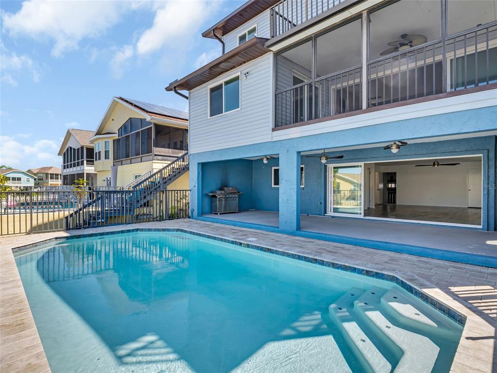 A swimming pool sits in front of a multi-story house with a covered patio and balcony — 6241 BAYSIDE DRIVE, NEW PORT RICHEY, FL