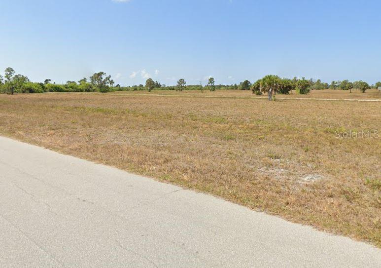 A paved road runs alongside a large, flat, grassy vacant lot under a clear blue sky — 12076 SEA-ROBIN LANE, PLACIDA, FL