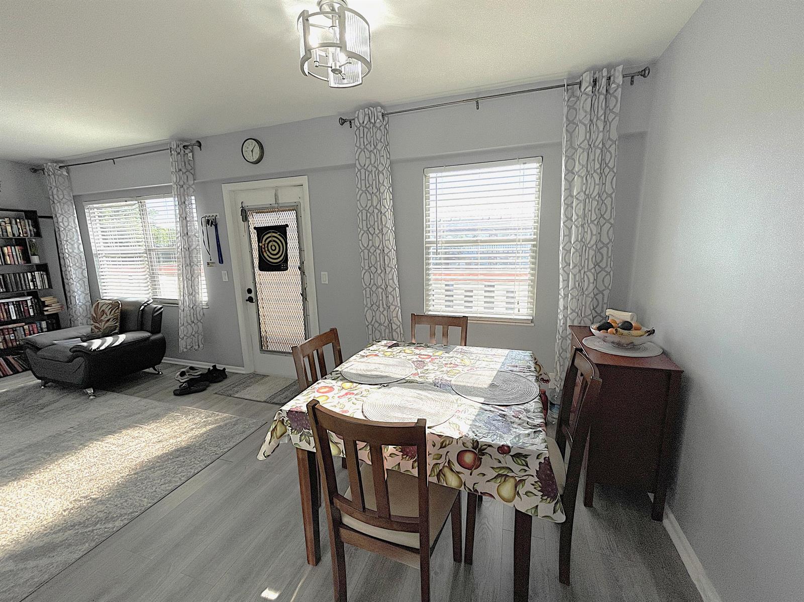 A dining area with a patterned tablecloth sits adjacent to a living room with bookshelves — 334 Brighton H, Boca Raton FL 33434, BOCA RATON, FL