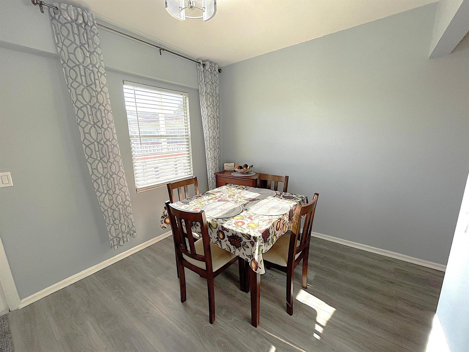 A dining room features light blue walls, gray wood-look flooring, and a window with curtains — 334 Brighton H, Boca Raton FL 33434, BOCA RATON, FL