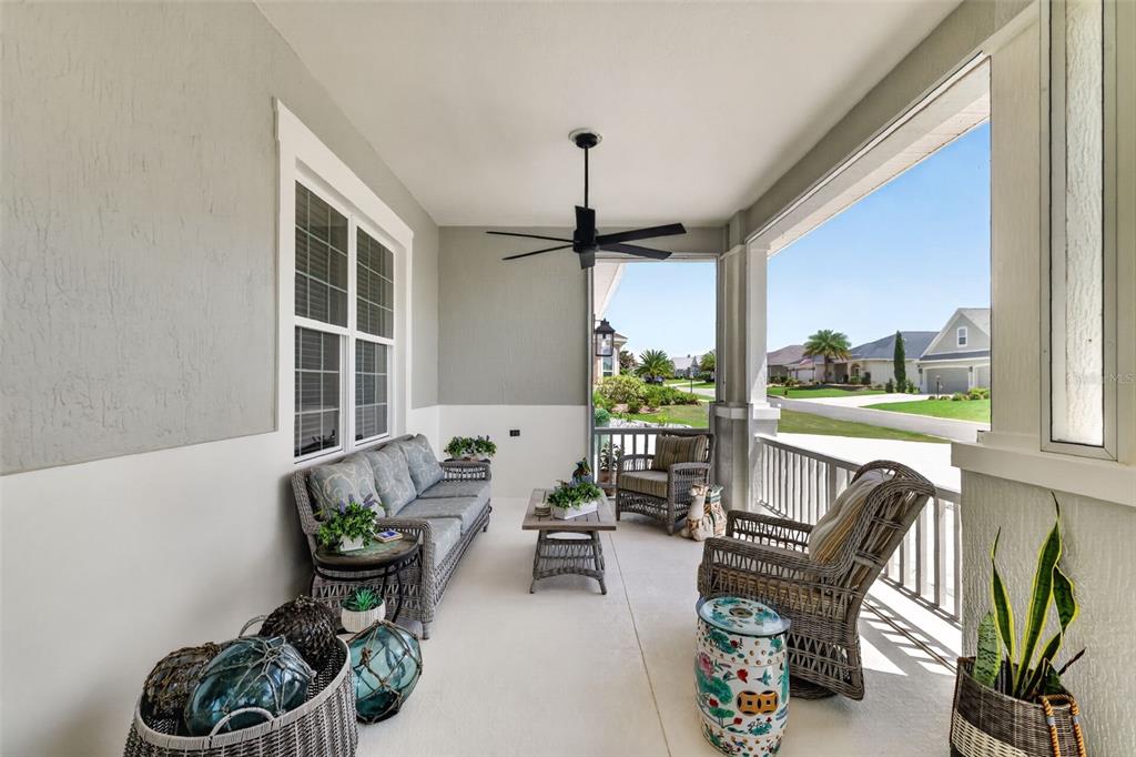 A covered patio features wicker furniture, a ceiling fan, and a view of suburban homes — 3468 MCDANIEL PLACE, THE VILLAGES, FL