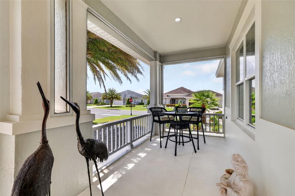 A covered porch features a small dining set, decorative bird statues, and views of neighborhood homes — 3468 MCDANIEL PLACE, THE VILLAGES, FL