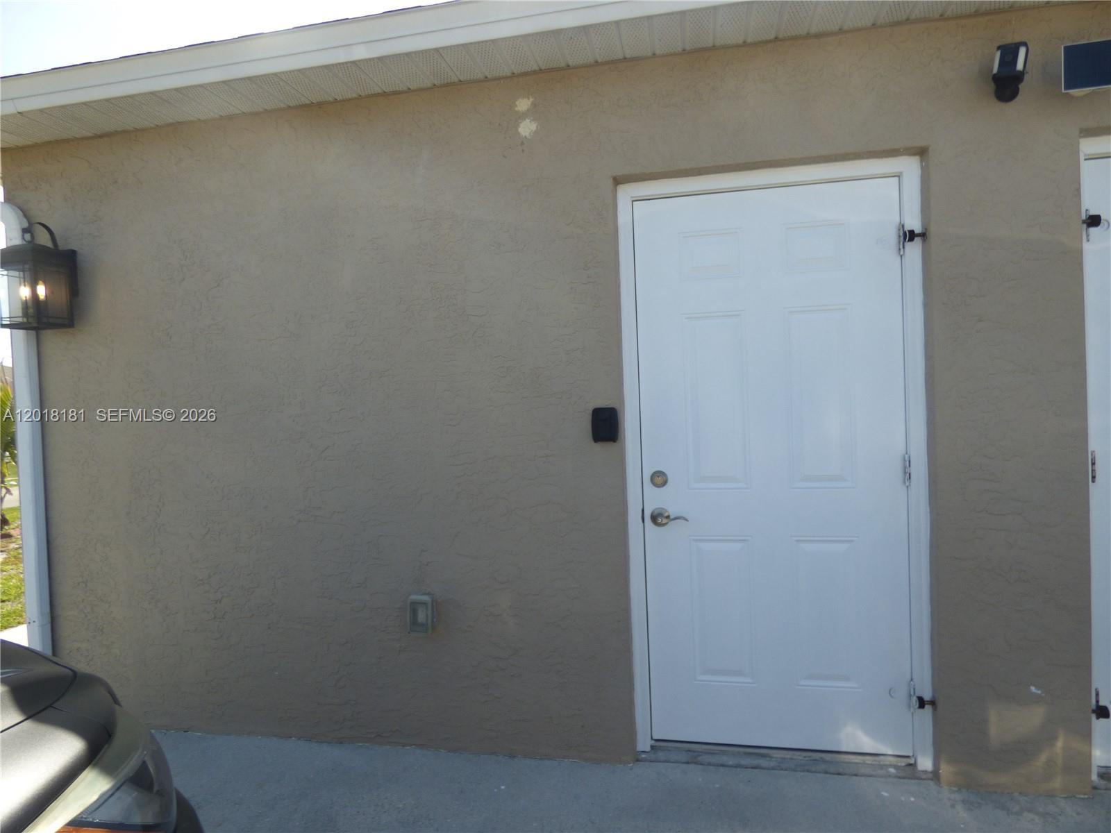 A white exterior door is set into a tan stucco wall with a wall-mounted lamp — PORT ST. LUCIE, FL