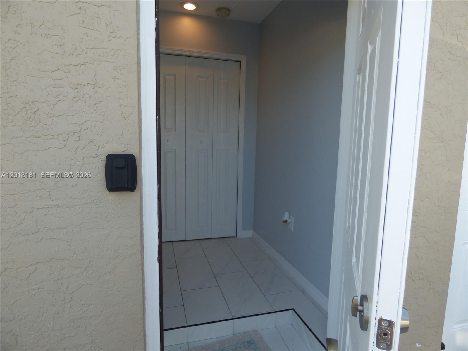 A view through an open doorway into a tiled entryway with a closet — PORT ST. LUCIE, FL