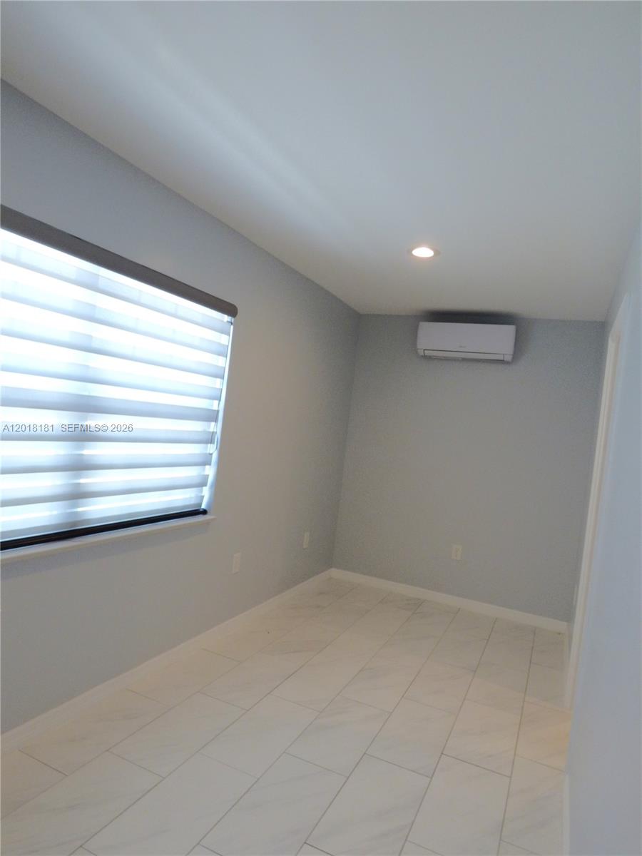 An empty room features light gray walls, white tile flooring, a window with blinds, and an air conditioner — PORT ST. LUCIE, FL