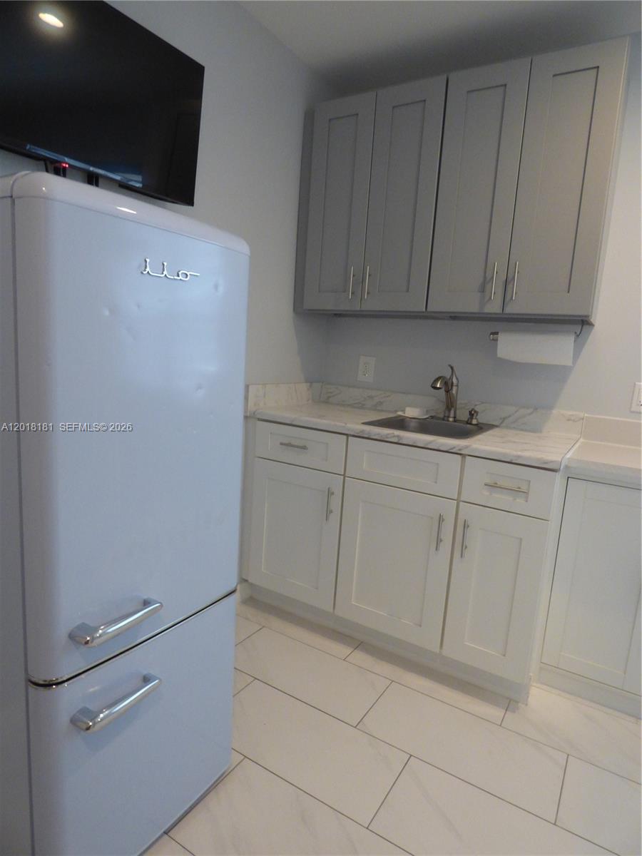A kitchenette features a retro-style refrigerator, gray upper cabinets, white lower cabinets, and a sink — PORT ST. LUCIE, FL