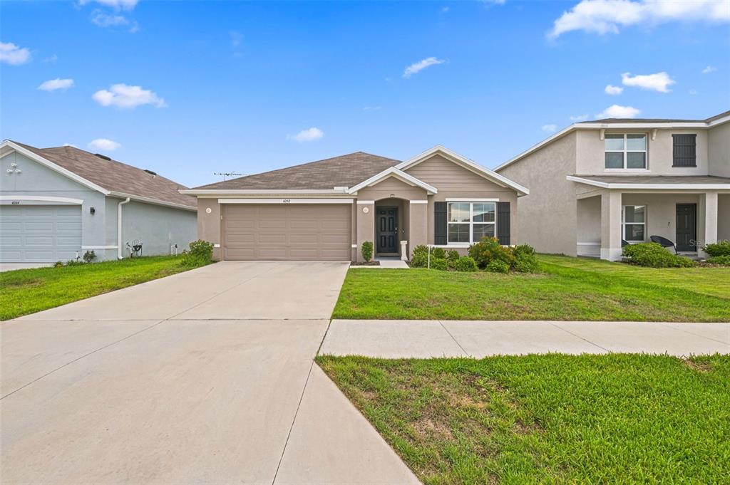 A single-story suburban house with a tan exterior, a two-car garage, and a front lawn — 4052 AUTUMN AMBER DRIVE, SPRING HILL, FL